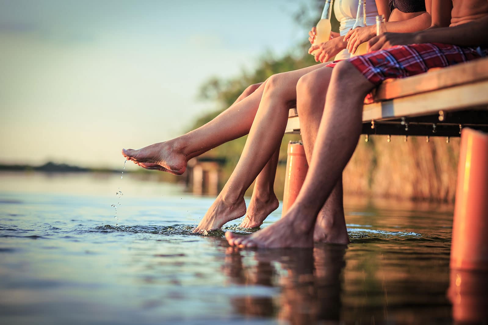 Shot of people's legs sitting on a dock with feet in water.