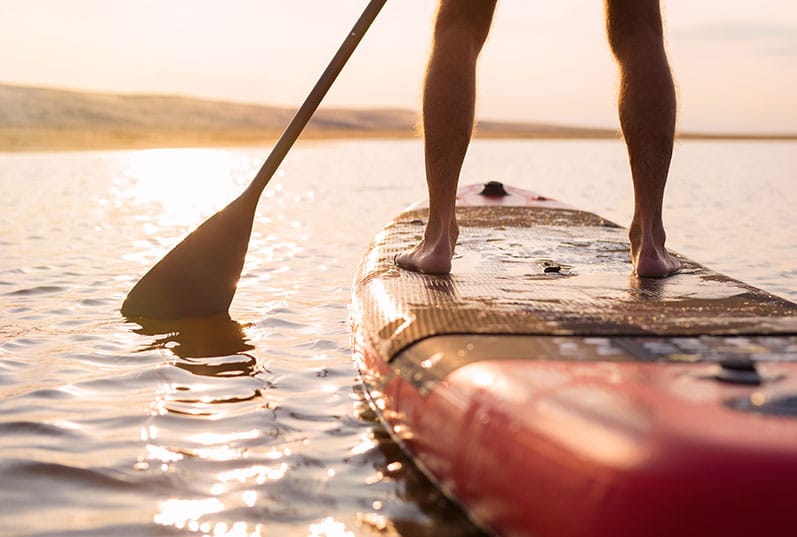 Man's Legs while paddle boarding at sunset